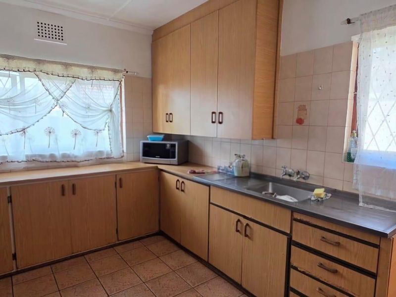A functional kitchen featuring laminate cabinetry, tiled backsplash, double sink, and tiled flooring, offering a classic layout with potential for modern updates.
