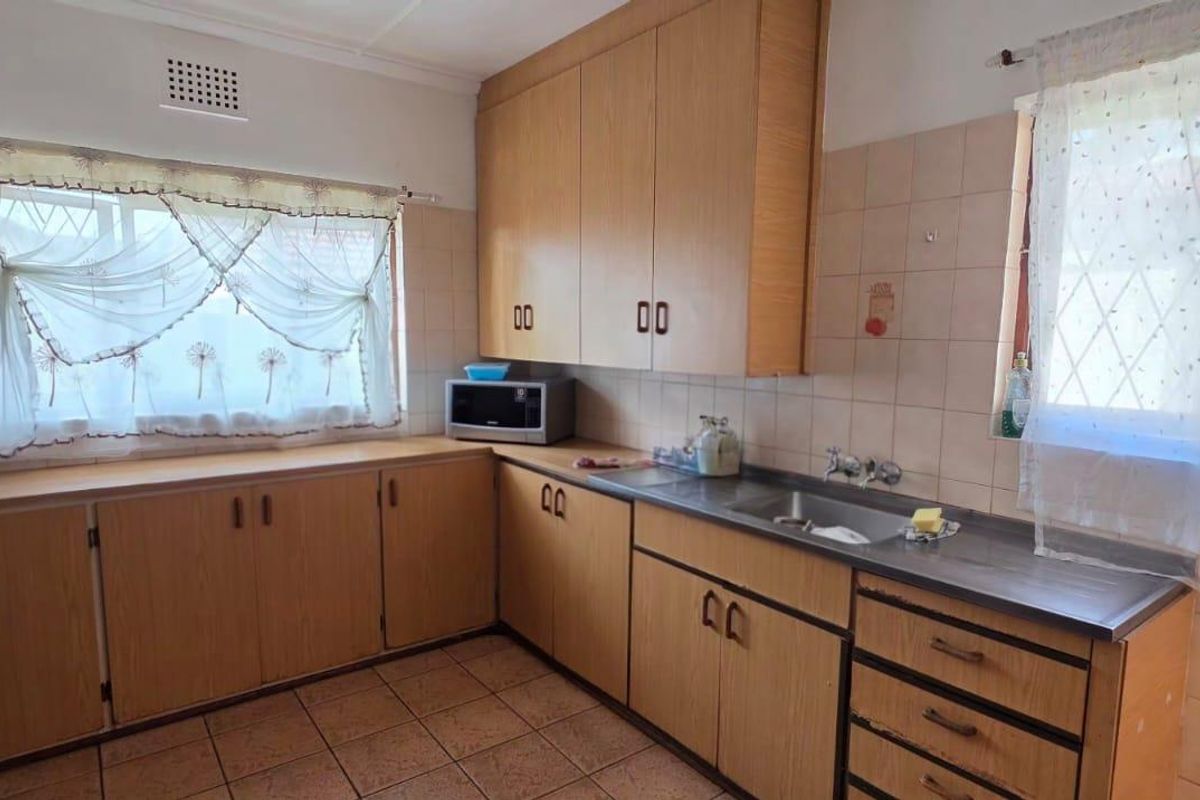 A functional kitchen featuring laminate cabinetry, tiled backsplash, double sink, and tiled flooring, offering a classic layout with potential for modern updates.