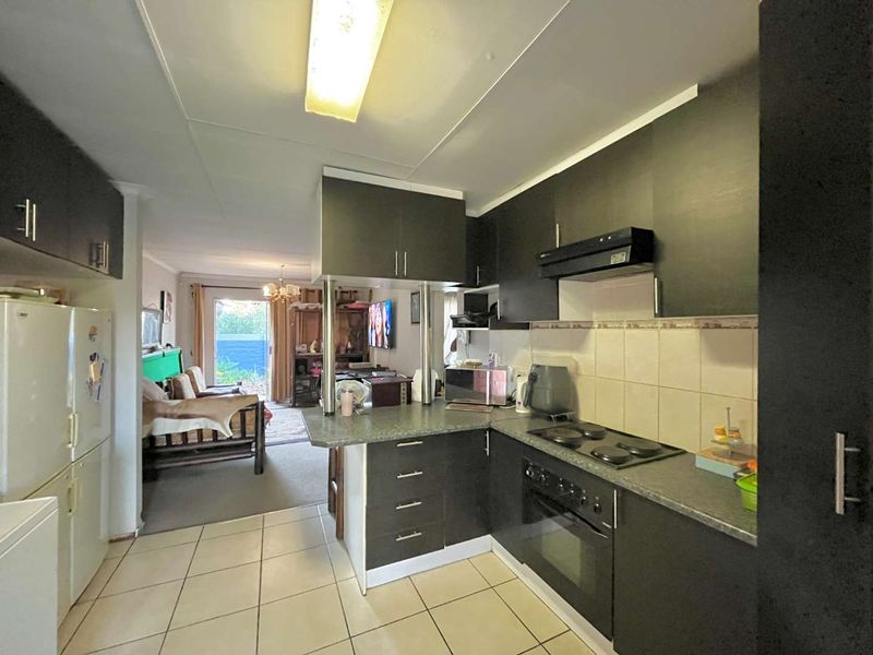 Open-plan kitchen featuring dark cabinetry, laminate countertops, and integrated appliances, flowing directly into the adjacent living area with access to the outdoors.