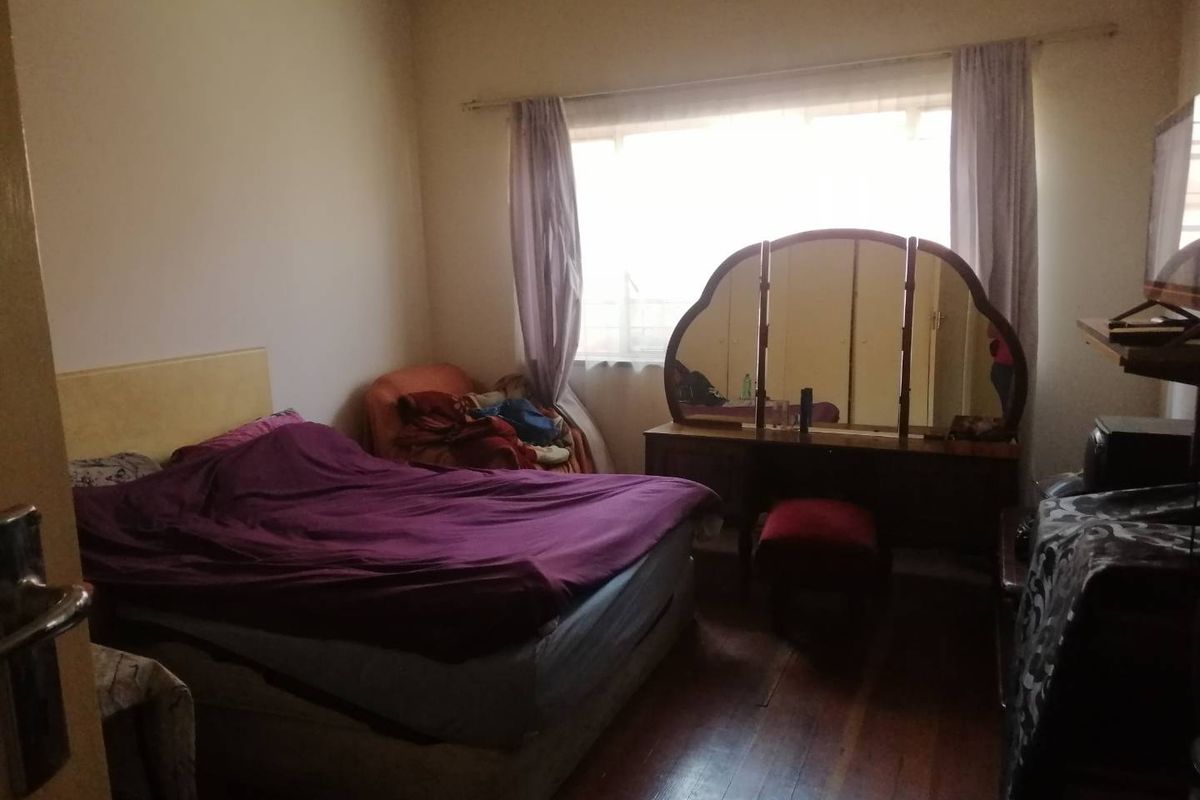 A bedroom featuring original timber flooring, a large window with curtain tracks, and a ceiling ventilation vent.