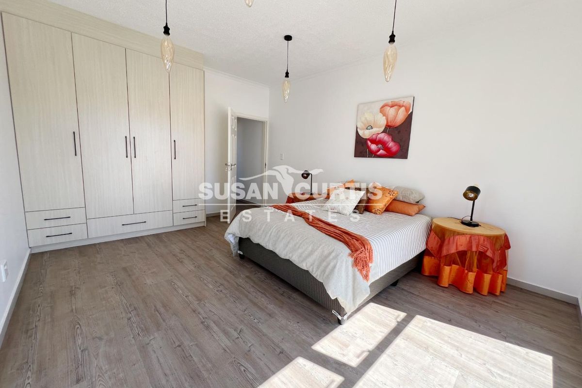 Spacious bedroom featuring light wood-look flooring, built-in floor-to-ceiling wardrobes, and modern pendant lighting.