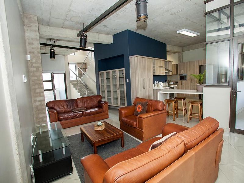 Spacious open-plan living area featuring an industrial-style exposed concrete ceiling, modern kitchen with breakfast bar, and a staircase leading to the upper level.
