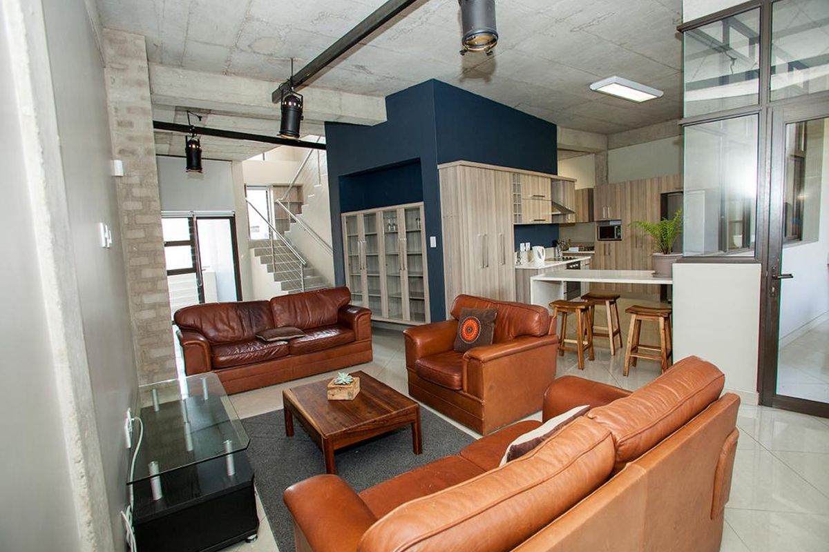 Spacious open-plan living area featuring an industrial-style exposed concrete ceiling, modern kitchen with breakfast bar, and a staircase leading to the upper level.