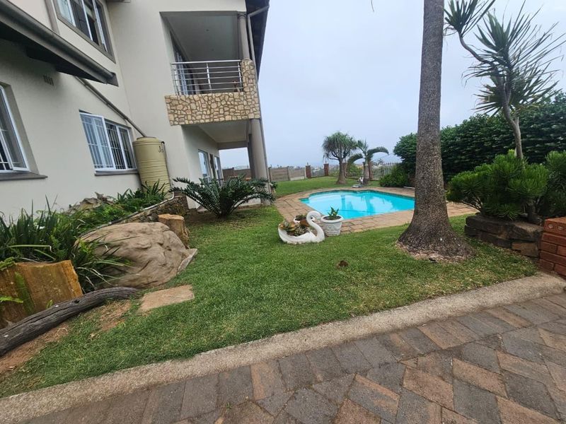 Rear exterior view featuring a swimming pool, landscaped garden, paved patio area, and a multi-story building with a balcony and stone cladding.