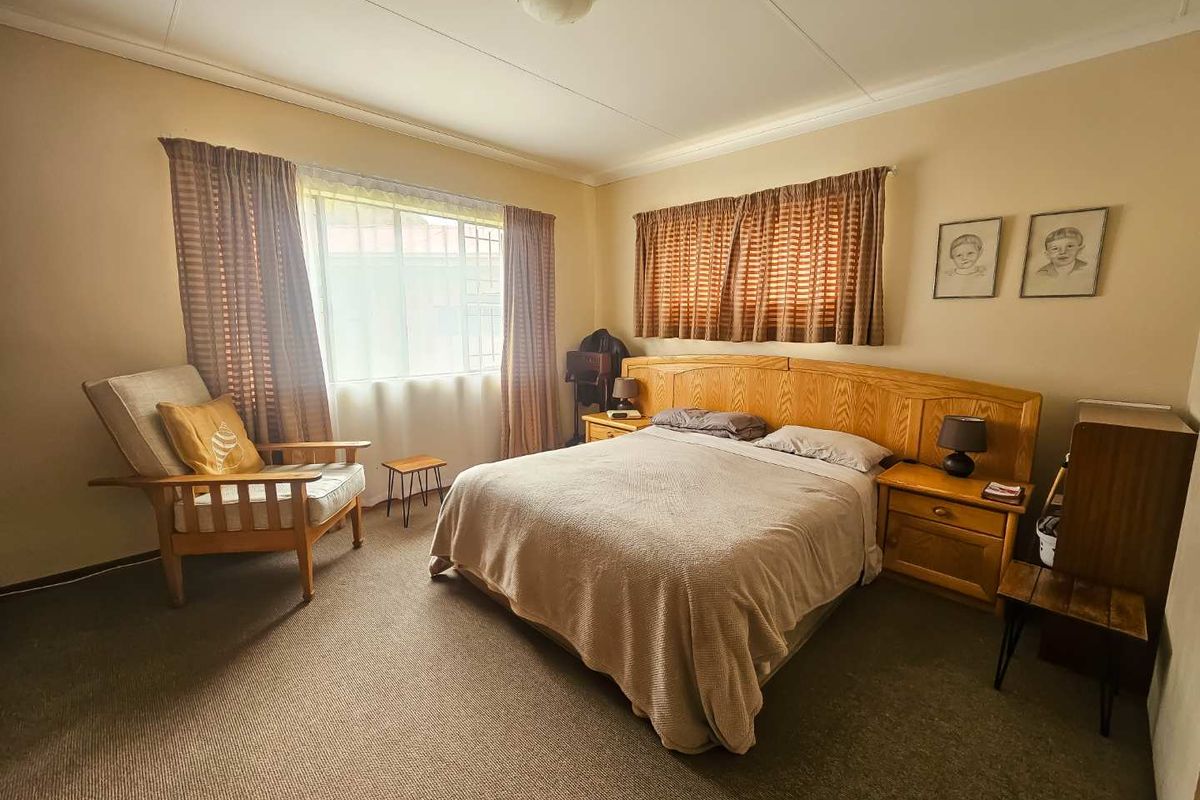 A spacious bedroom featuring neutral walls, carpeted flooring, and large windows with curtains, providing a comfortable and functional living space.