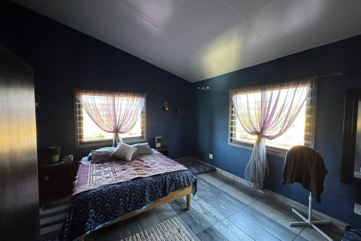 A spacious bedroom featuring dark blue walls, tiled flooring, and dual windows with natural light, offering a cozy and private atmosphere.