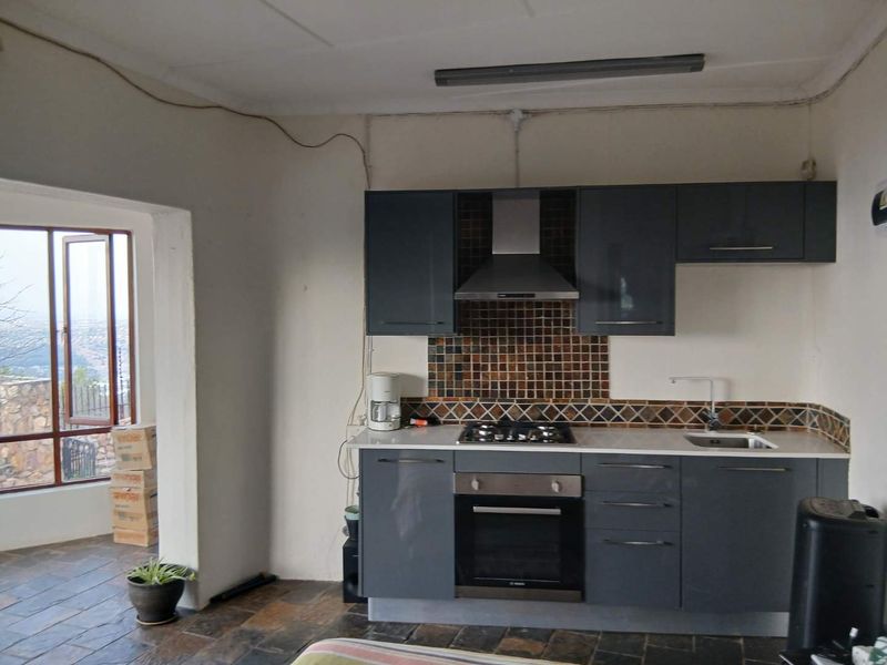 Compact kitchen featuring dark grey cabinetry, gas hob, built-in oven, mosaic tile backsplash, and slate flooring, with direct access to an outdoor area.
