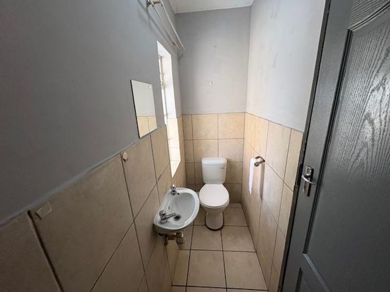 A compact guest bathroom featuring a wall-mounted basin and toilet with neutral tiled finishes, requiring minor cosmetic updates to improve its overall presentation.