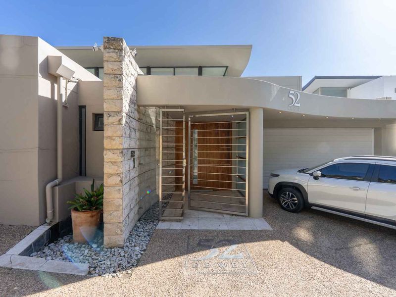 Modern front facade featuring a striking stone feature wall, stainless steel security gate, and a contemporary timber pivot entrance door.