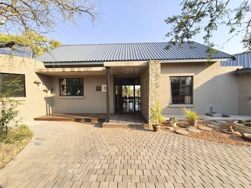 Front elevation of a modern house featuring a metal roof, stone cladding accents, timber decking at the entrance, and a paved driveway.
