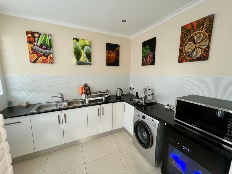 A functional scullery featuring white cabinetry, black stone benchtops, a double bowl stainless steel sink, and a mosaic tile splashback.