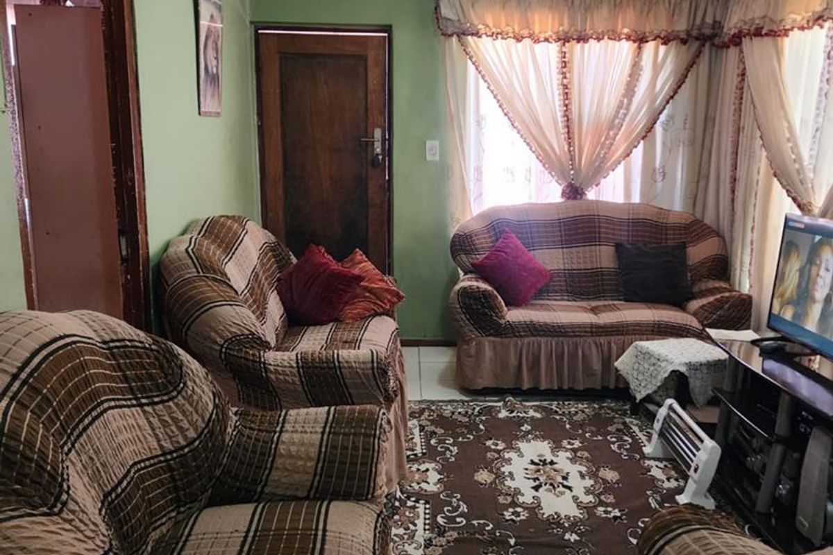 A living room featuring tiled flooring, textured ceiling with coving, and a timber door, presenting an opportunity for cosmetic updates.
