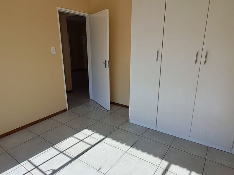 A clean, empty bedroom featuring neutral wall paint, tiled flooring, and a built-in wardrobe with white cabinetry.
