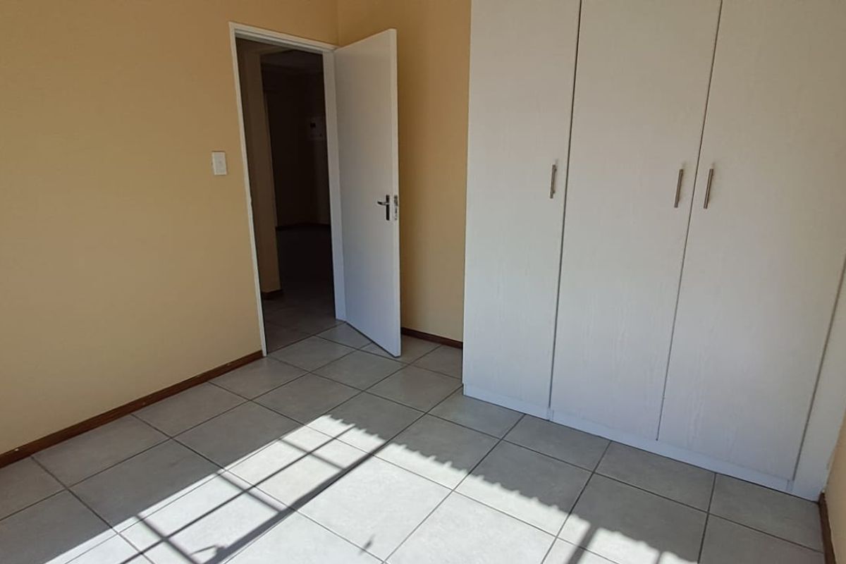 A clean, empty bedroom featuring neutral wall paint, tiled flooring, and a built-in wardrobe with white cabinetry.