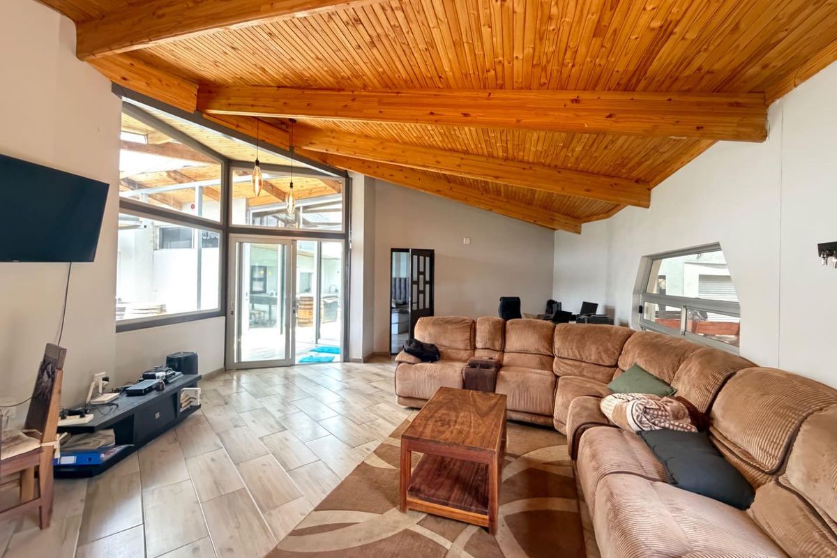 Spacious living room featuring a high exposed timber raked ceiling, tiled flooring, and large glass doors providing natural light and access to the patio.