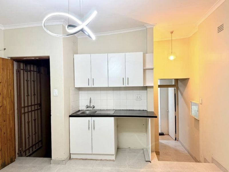 Compact kitchen area featuring white built-in cabinetry, a dark laminate countertop, stainless steel sink, and tiled backsplash, ready for final finishing touches.