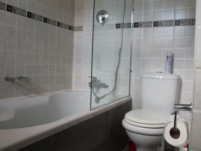 A functional bathroom featuring a bathtub with a glass shower screen, wall-mounted shower mixer, and a standard toilet with tiled wall finishes.