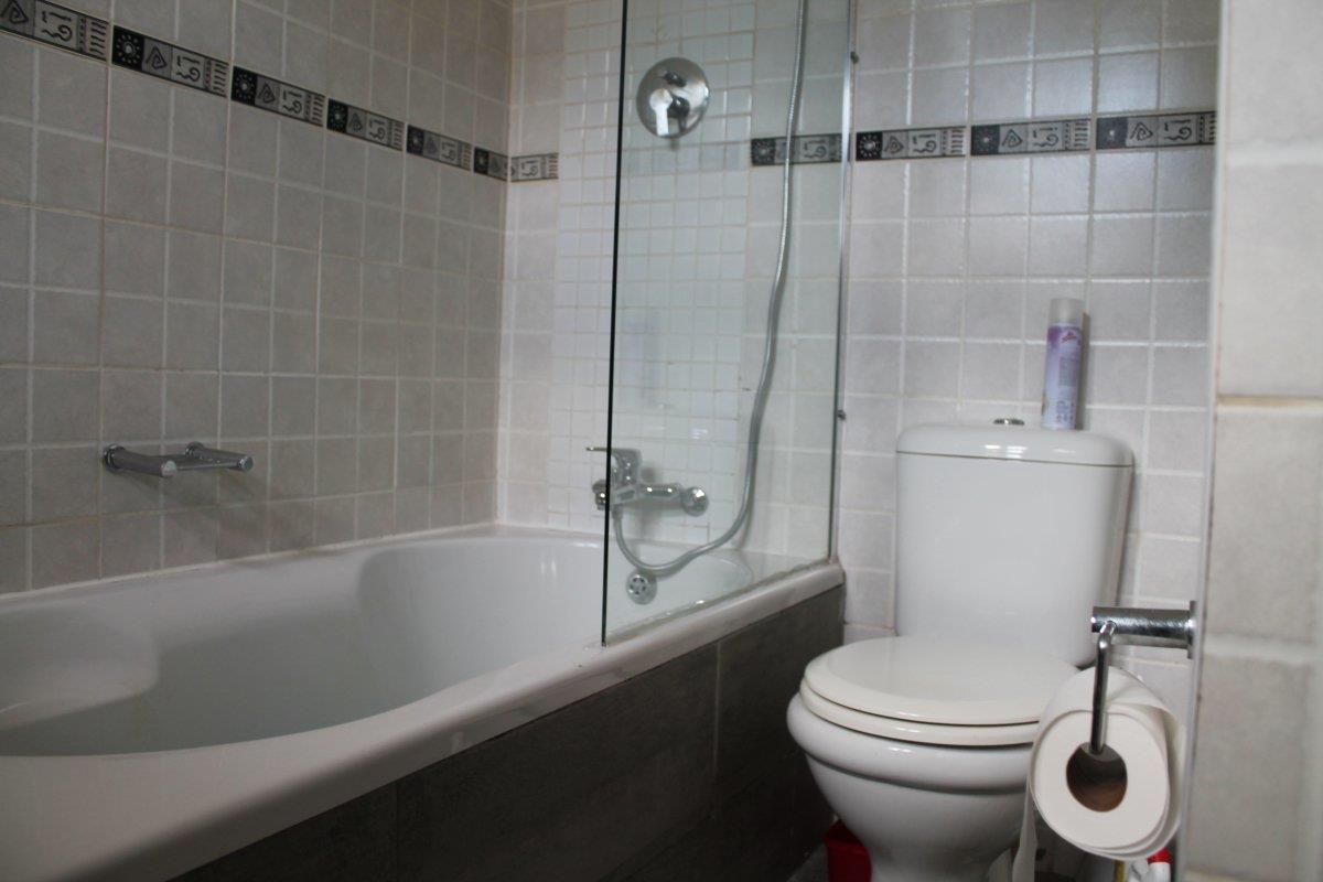 A functional bathroom featuring a bathtub with a glass shower screen, wall-mounted shower mixer, and a standard toilet with tiled wall finishes.