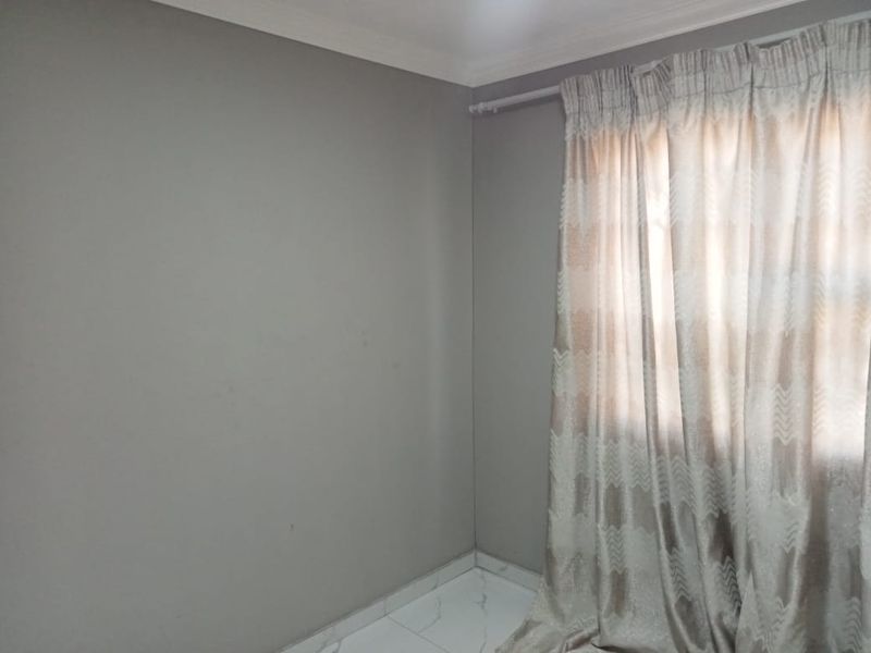 A simple, empty bedroom featuring neutral grey walls, tiled flooring, and a curtain rod, offering a clean canvas for personalization.