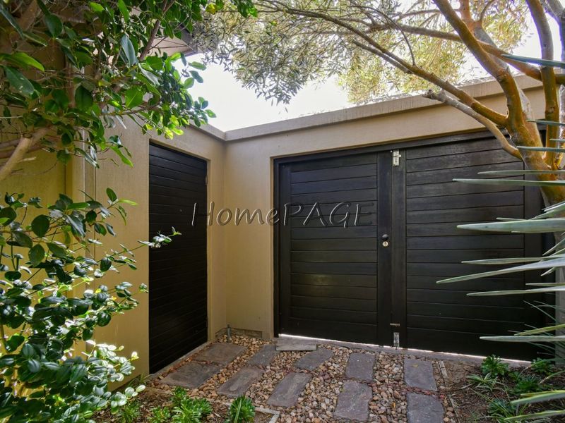 A private rear courtyard area featuring dark timber gates, a side access door, and stone-paved pathways set within a landscaped garden.