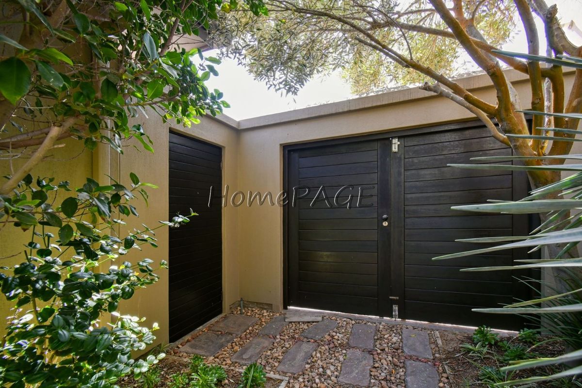 A private rear courtyard area featuring dark timber gates, a side access door, and stone-paved pathways set within a landscaped garden.