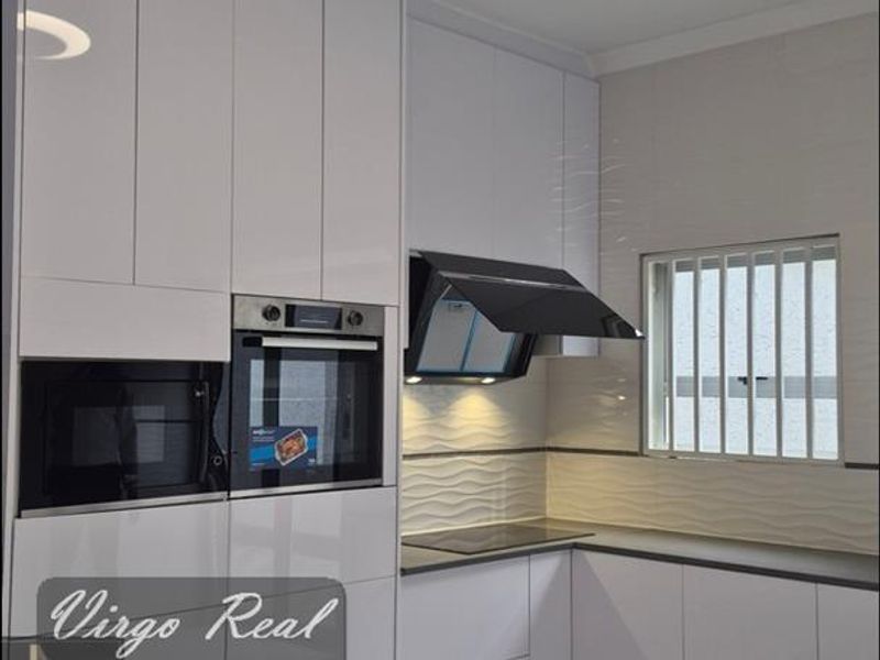 Modern kitchen featuring high-gloss white cabinetry, built-in oven and microwave, sleek hob with extractor fan, and contemporary textured backsplash tiling.