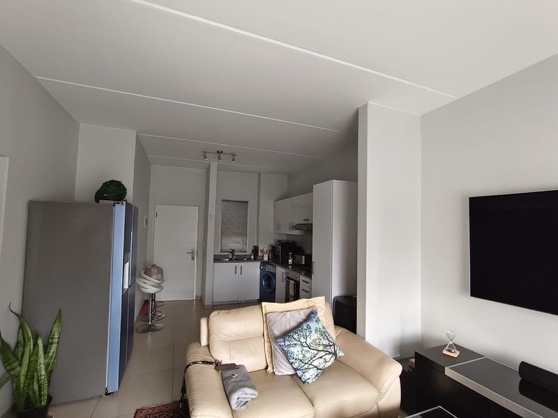 Open-plan living area featuring a compact kitchen with built-in cabinetry, tiled flooring, and neutral wall finishes, creating a functional and cohesive space.