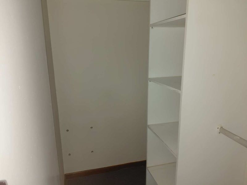 A small walk-in closet or storage area featuring built-in white shelving and a hanging rail, currently vacant.