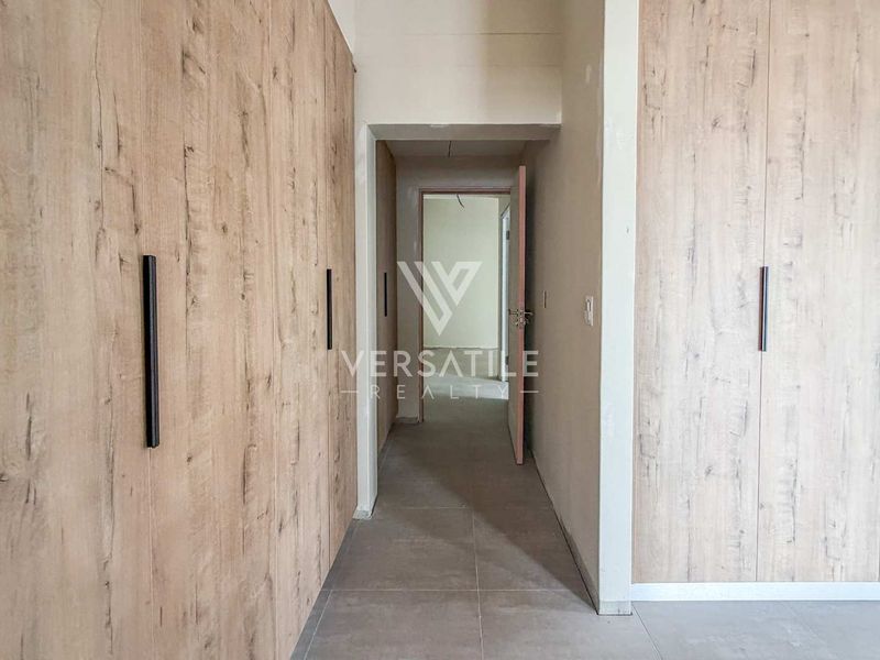 A clean, modern hallway featuring light wood-grain built-in cupboards and neutral floor tiles, leading to an adjacent room.