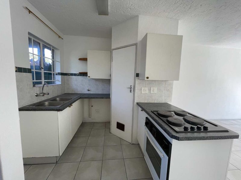A functional, empty kitchen featuring white cabinetry, dark laminate countertops, a built-in oven, and an electric hob with tiled backsplash and flooring.
