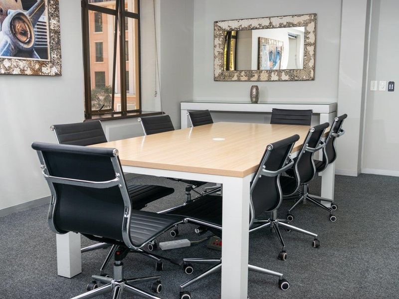 A professional office meeting room featuring neutral walls, carpeted flooring, and a large window providing natural light.