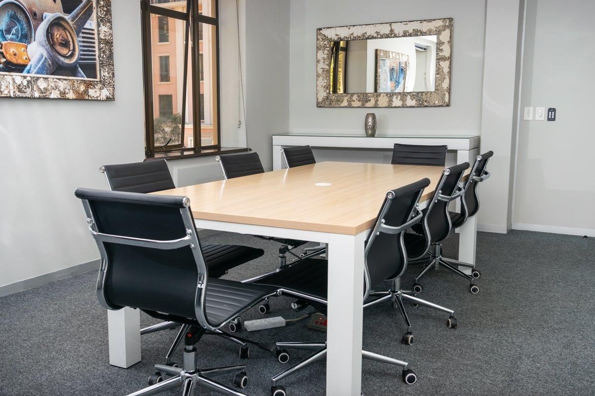 A professional office meeting room featuring neutral walls, carpeted flooring, and a large window providing natural light.