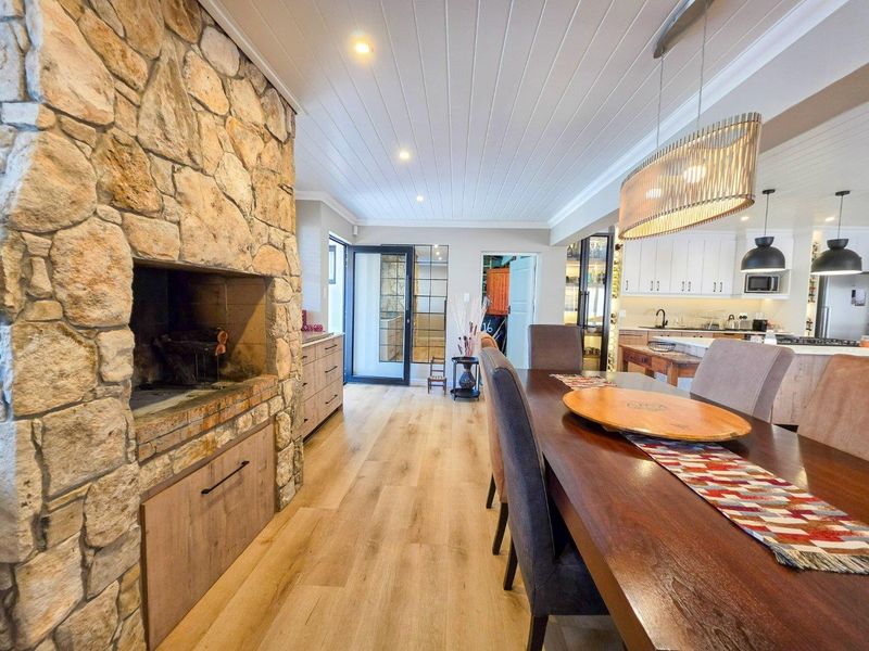 Spacious open-plan living and dining area featuring a prominent stone fireplace, timber flooring, and a modern kitchen with integrated cabinetry and pendant lighting.