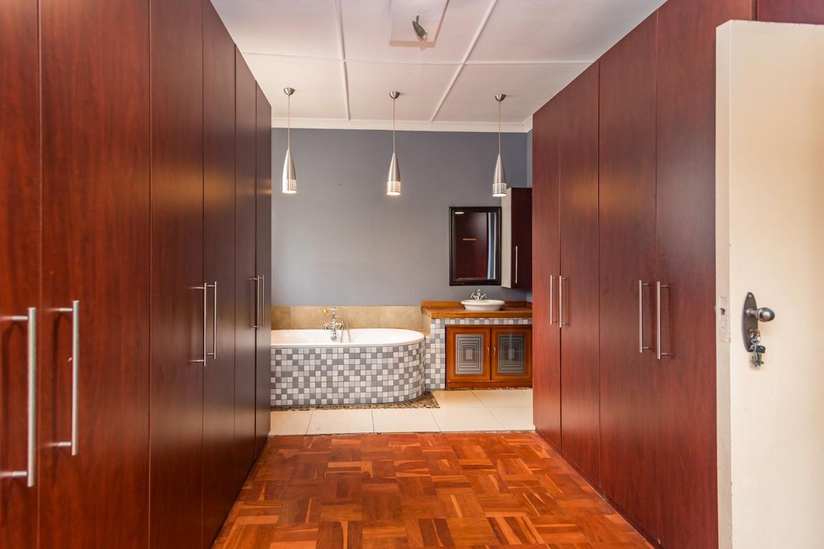 A spacious bathroom featuring extensive built-in cabinetry, a tiled bathtub surround, a vanity with a vessel sink, and warm parquet flooring.