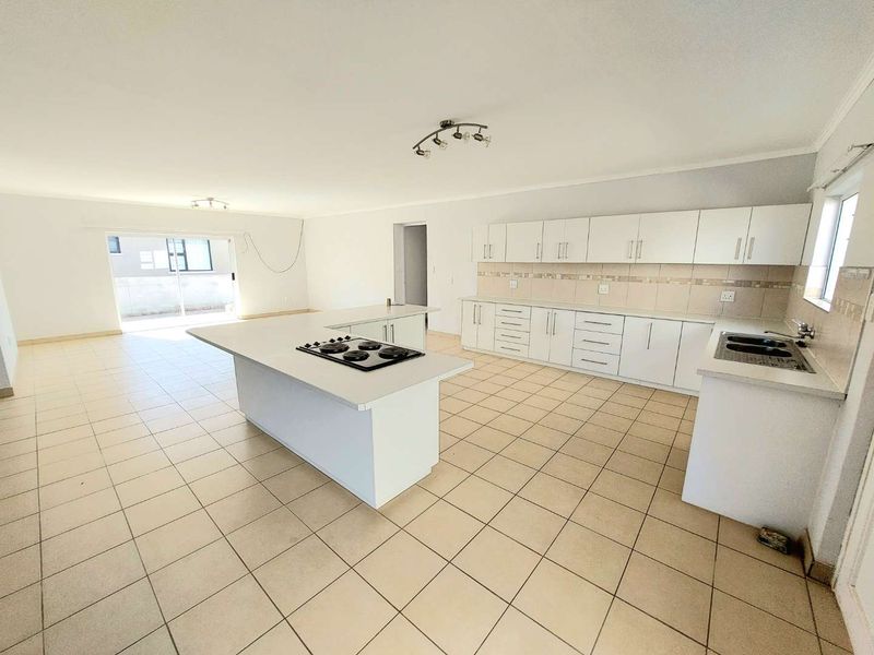 Spacious open-plan kitchen and living area featuring tiled floors, ample built-in cabinetry, a central island with a hob, and sliding doors to the exterior.