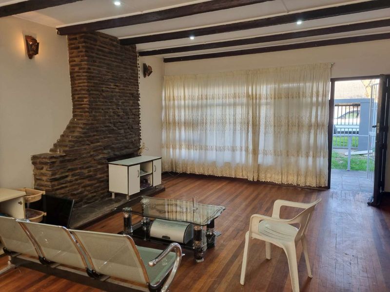 Spacious living room featuring exposed timber ceiling beams, a prominent stone fireplace, and hardwood flooring, with direct access to the exterior.