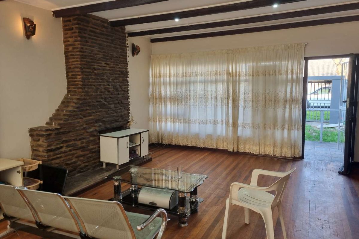 Spacious living room featuring exposed timber ceiling beams, a prominent stone fireplace, and hardwood flooring, with direct access to the exterior.