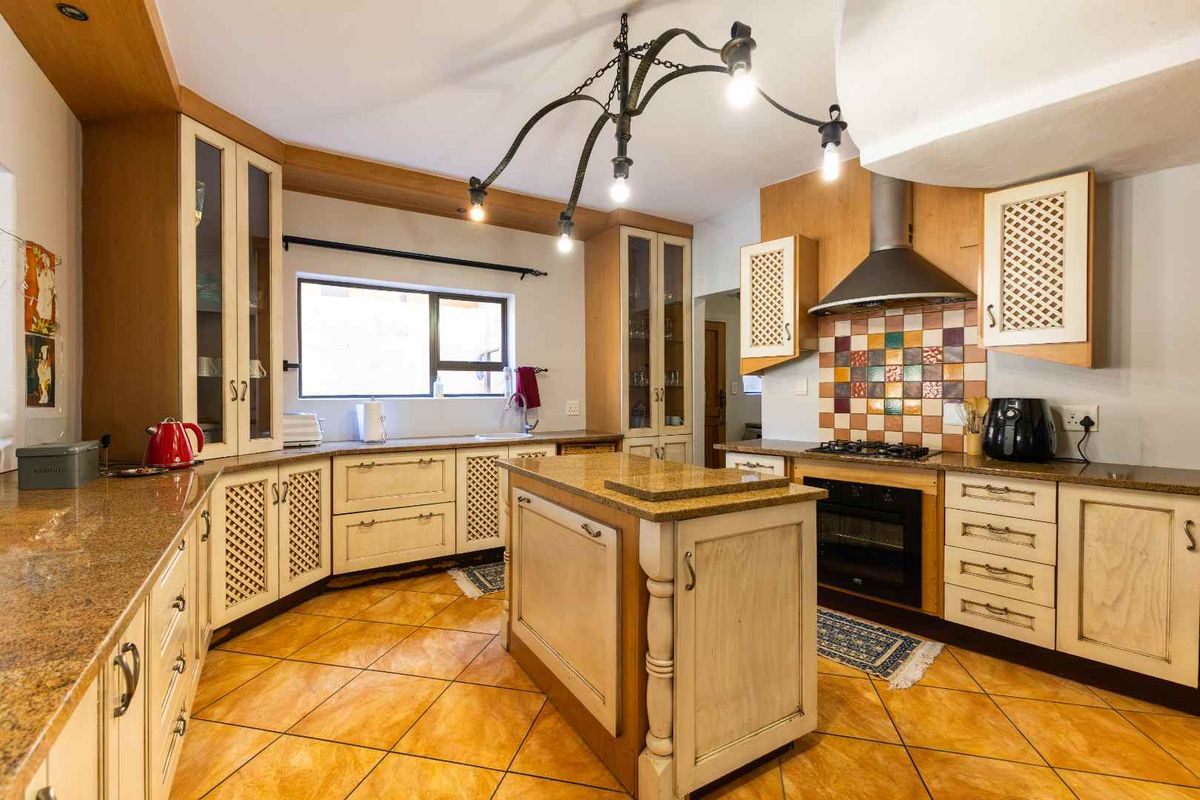 Spacious kitchen featuring granite countertops, a central island, built-in oven with gas hob, extractor fan, and ample custom cabinetry with tiled flooring.