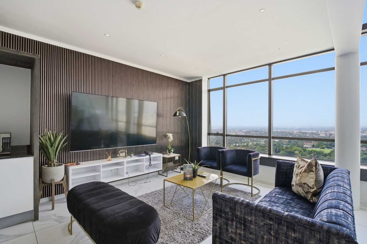 Modern living room featuring floor-to-ceiling windows with expansive city views, sleek slatted feature wall, and polished tile flooring.