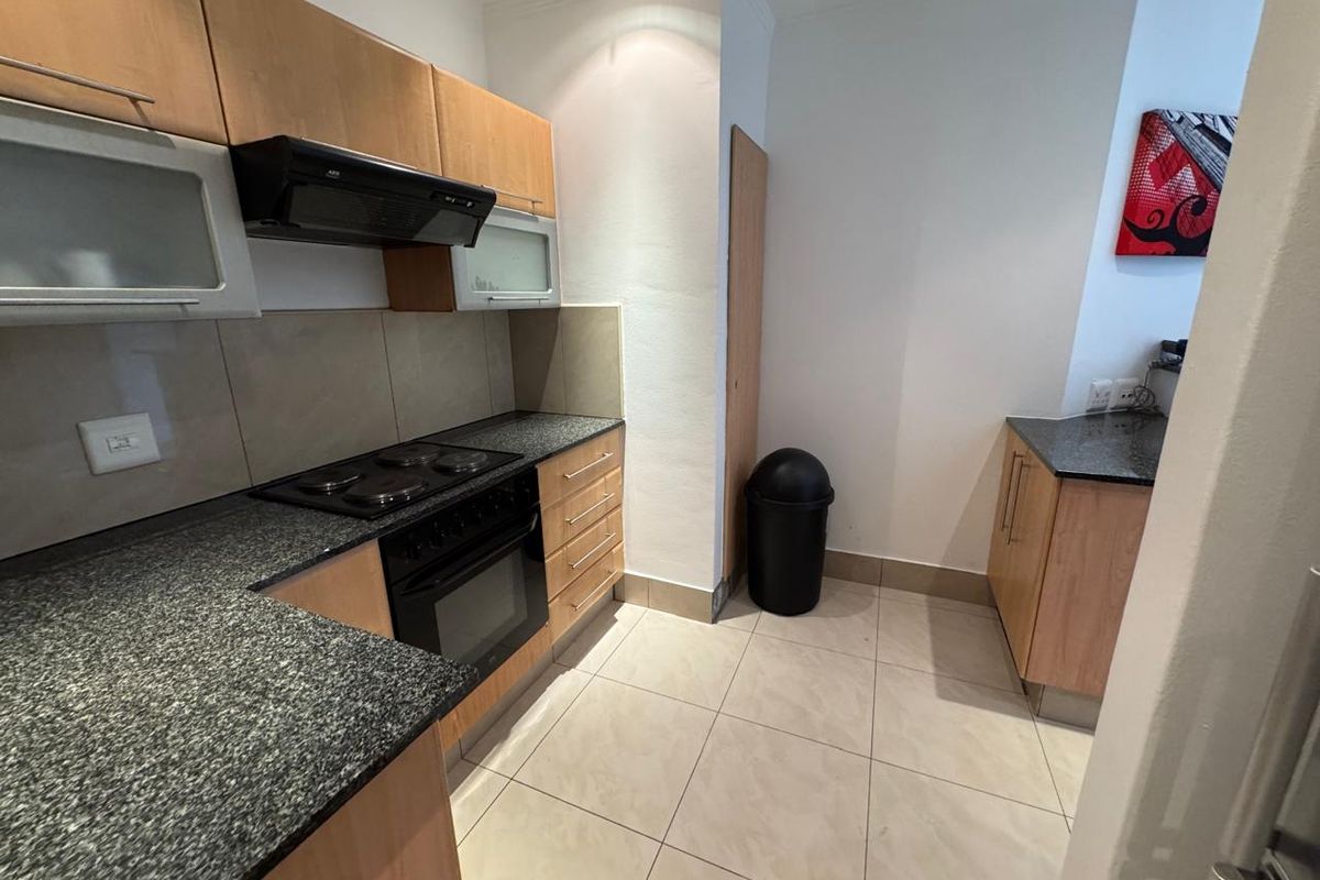 A functional kitchen featuring light wood cabinetry, granite countertops, a built-in oven, electric hob, and neutral tiled flooring.