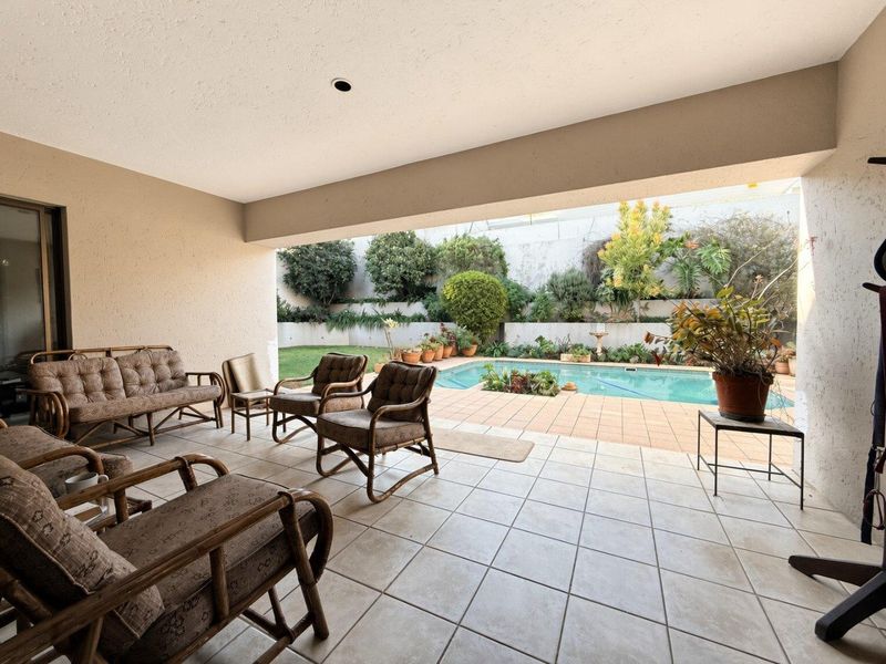 Covered patio area overlooking a swimming pool and landscaped garden with tiered retaining walls.