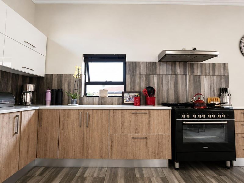 Modern kitchen featuring wood-look lower cabinetry, white upper cabinets, stone-look backsplash, and a black freestanding oven with matching extractor fan.