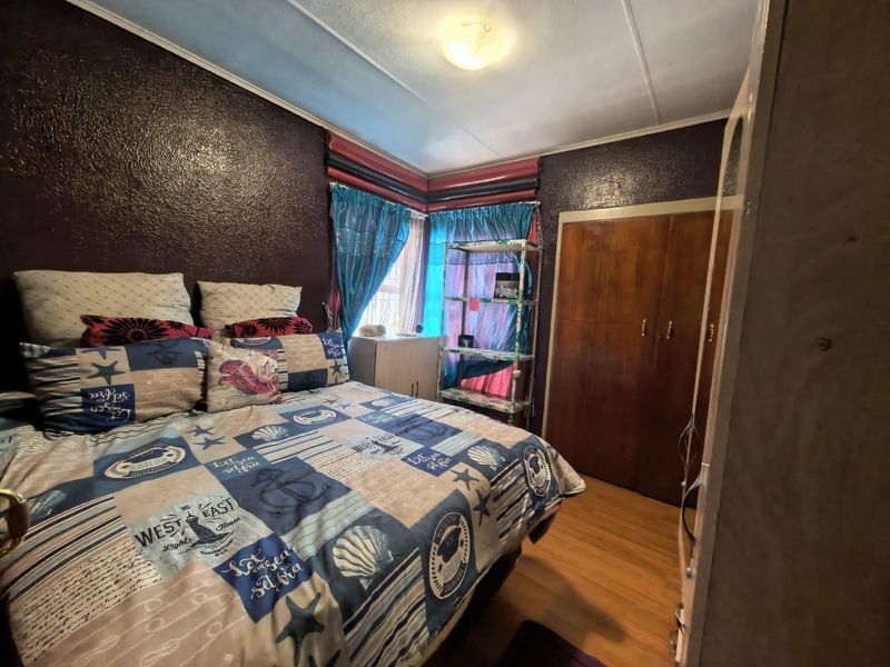 A bedroom featuring laminate flooring and a built-in wooden wardrobe, currently finished with dark textured wall paint.