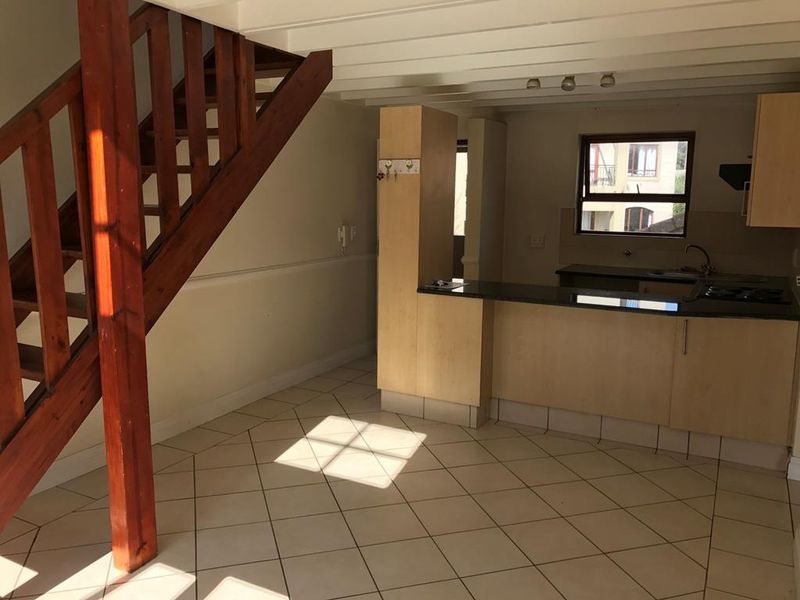 Open plan living area featuring a wooden staircase, tiled flooring, and a functional kitchen with granite countertops and built-in cabinetry.