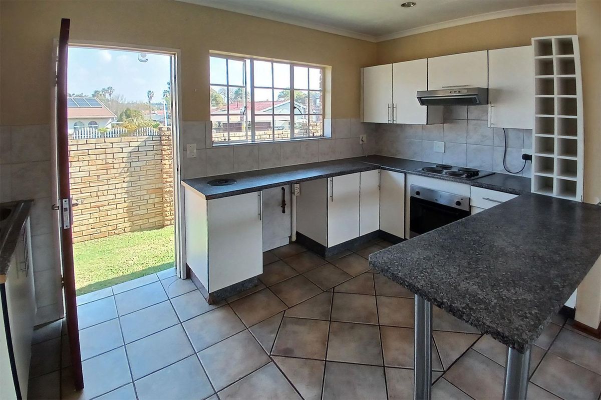 A functional kitchen featuring white cabinetry, dark laminate countertops, built-in oven and hob, tiled flooring, and direct access to the rear garden.