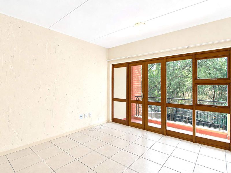 A bright, empty living area featuring neutral tiled flooring and large timber-framed glass doors that open onto a private balcony.