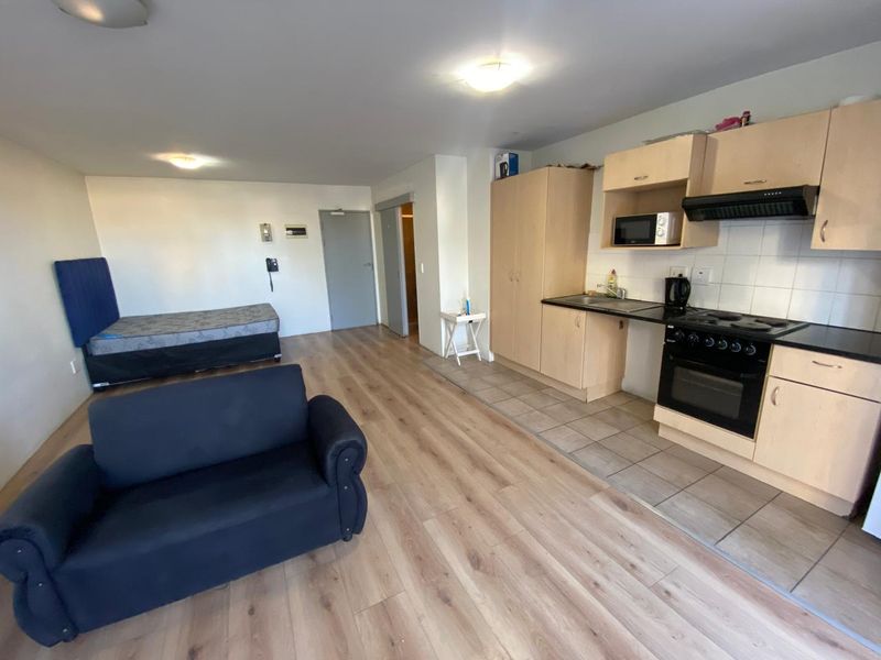 Open-plan studio apartment featuring a functional kitchen with built-in cabinetry, electric oven, and hob, seamlessly integrated with the living and sleeping area.