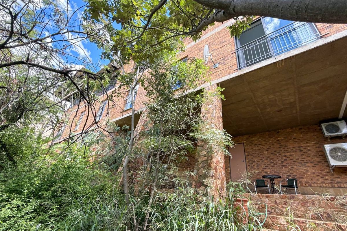 A view of the rear exterior facade featuring exposed brickwork, stone-clad pillars, a covered patio area, and balcony access.