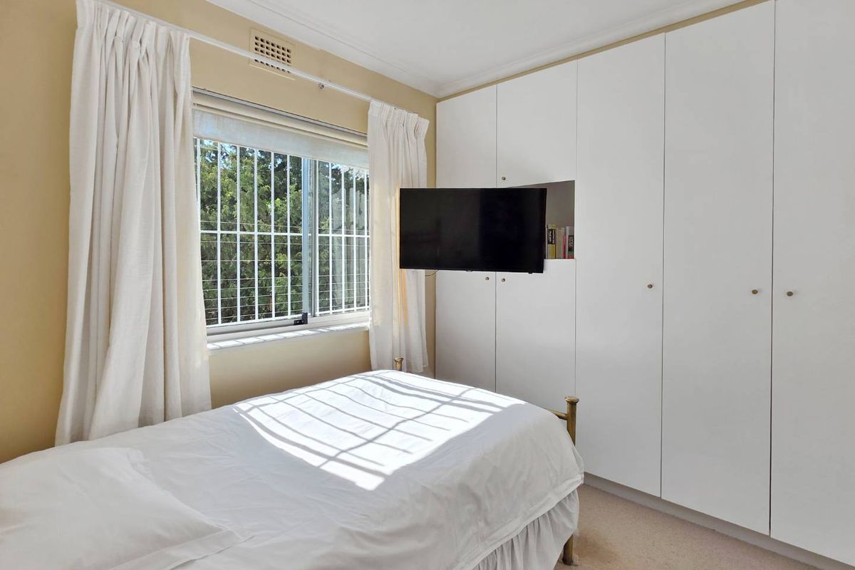 A bedroom featuring floor-to-ceiling built-in cupboards, a window with security bars, and neutral wall finishes.