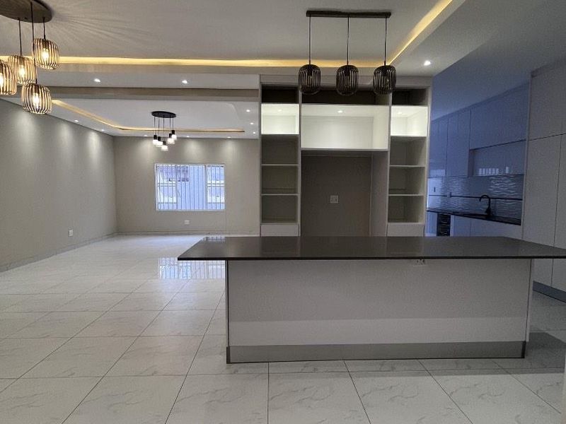 Spacious open-plan living and kitchen area featuring modern tiled flooring, recessed ceiling lighting, and a central kitchen island with built-in cabinetry.